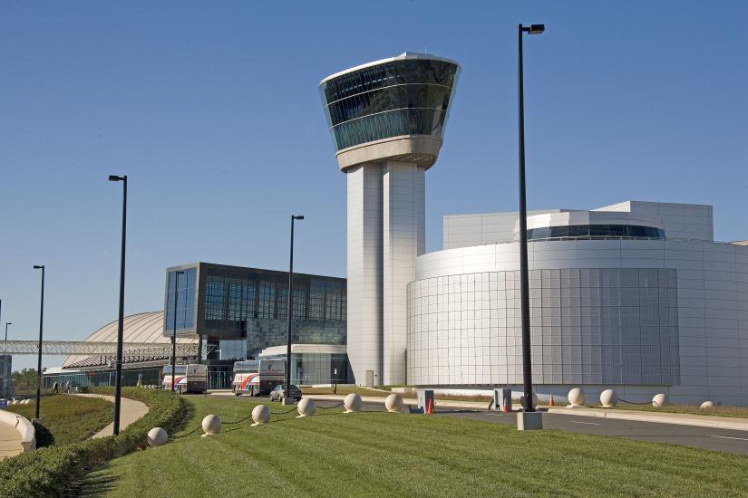 One side of large silver building with circular theater in foreground and Tower with glass-enclosed observation deck at top.