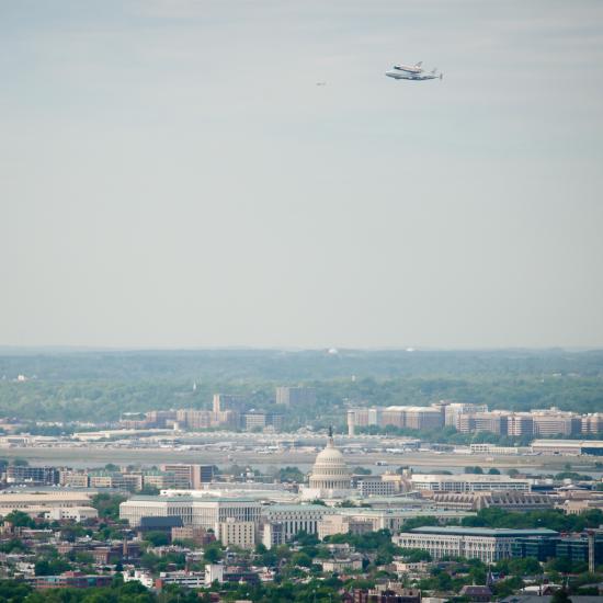 The Space Shuttle Discovery, attached to an aircraft modified for transporting shuttles, flies over the United States Capitol.