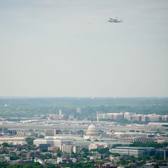 The Space Shuttle Discovery, attached to a modified aircraft used for shuttle transport, flies over Washington, DC.