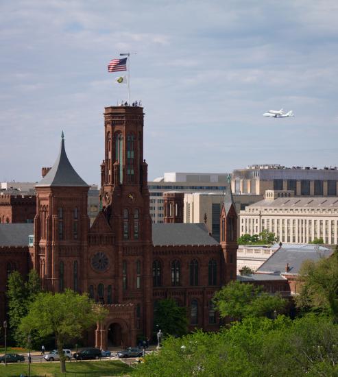 Space Shuttle Discovery, attached to an aircraft modified for shuttle transportation, flies near the Smithsonian Castle in Washington, D.C.