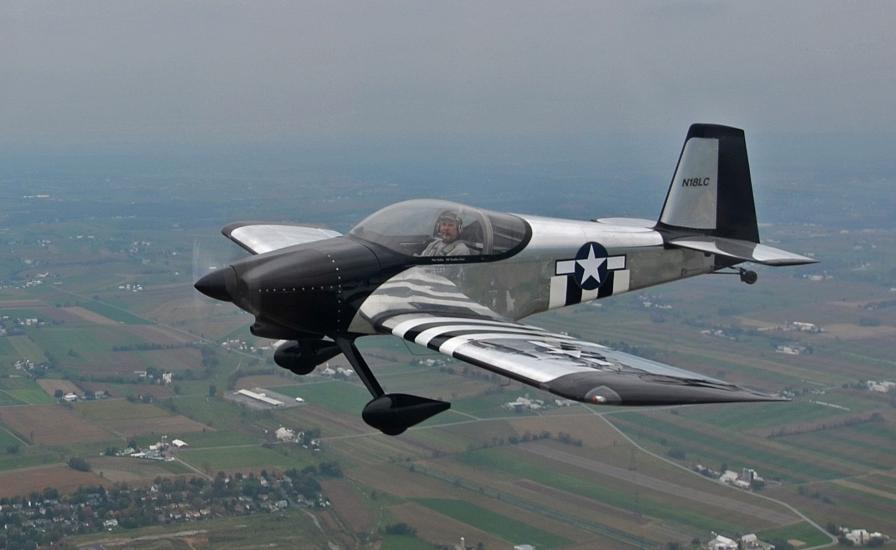 Side view of silver-colored, black, and white aircraft flying in the air with nonretractable landing gear.