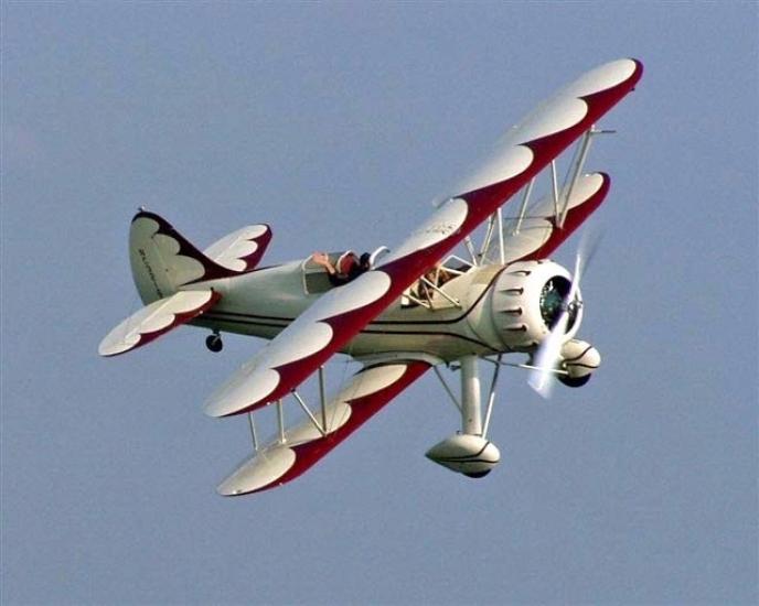 Side view of white and red biplane in flight with single engine.