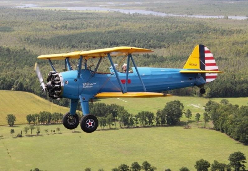 Side view of blue biplane with yellow wings and single engine during flight.