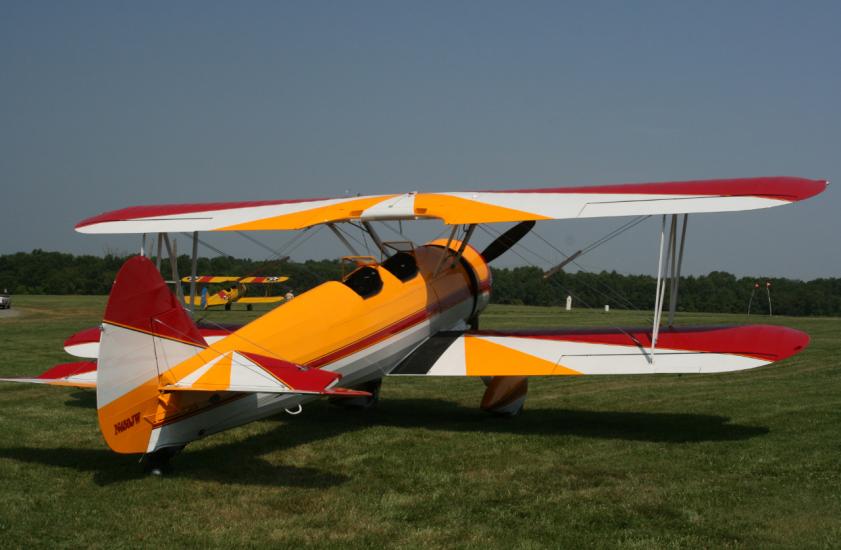 Back view of yellow, red, and white biplane with single engine.