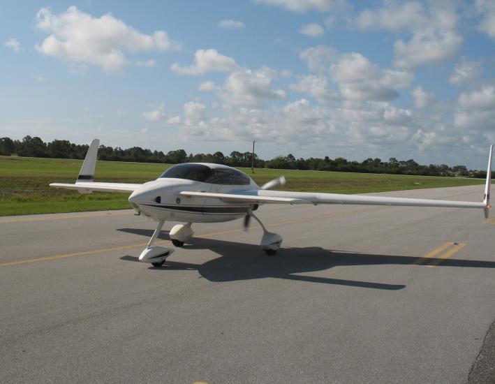 Frontal view of white monoplane with long wings and fixed landing gear.