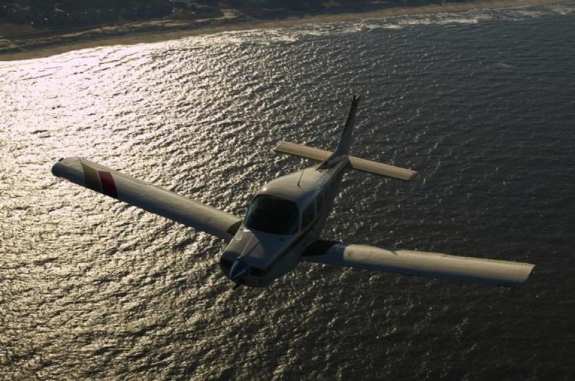 Front view of a monoplane with one engine flying above a body of water.