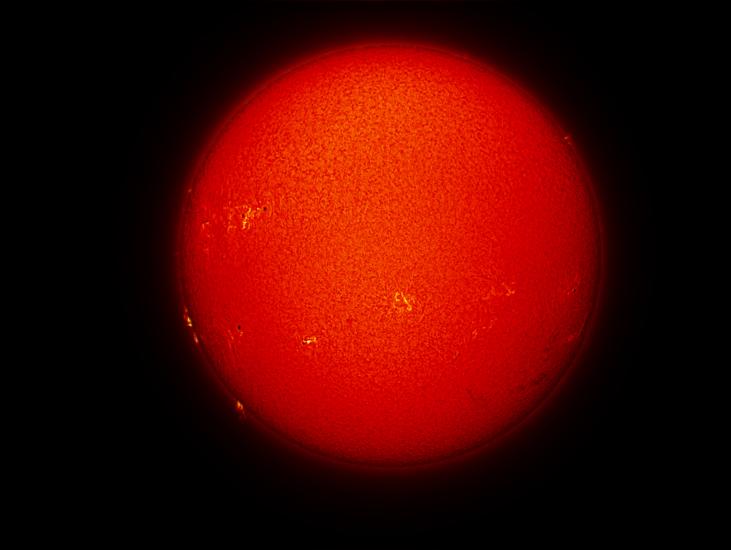 Disk view of the Sun's chromosphere with multiple sunspots and prominences of plasma rising from the chromosphere on the left side of the disk. Additional filaments of plasma floating above the chromosphere are visible on the bottom right quadrant of the disk.