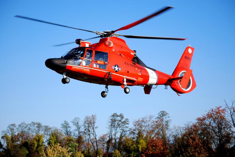 Side view of red helicopter with four blade propellor flying in the air.