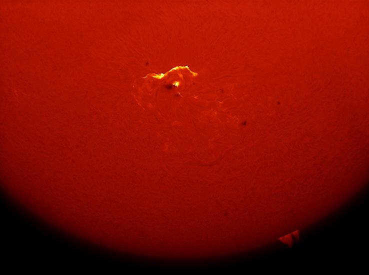 Partial disk view of the Sun focusing on a solar flare, highlighted in yellow with nearby black darkspots, visible from an image of the chromosphere of the Sun.