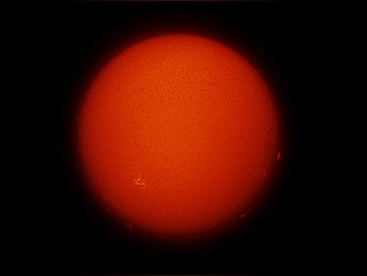 Disk view of the Sun with one visible sunspot cluster, highlighted in a yellow colour, and small prominences floating off the Sun across the bottom half of the visible Sun.