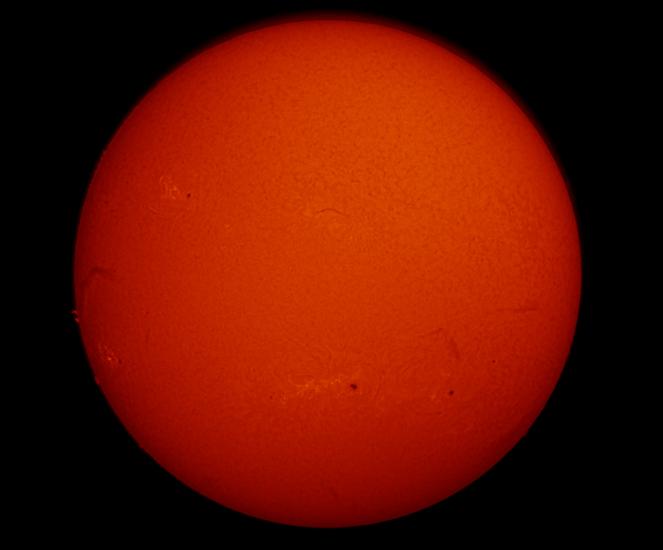 Disk view of the Sun's chromosphere. The left side of the disk features a dark line of gases floating above the Sun's surface known as a filament turn into a prominence as it moves beyond the end of the disk. Multiple sunspots, highlighted as dark marks, and phages, lighter sections, are found throughout the disk.