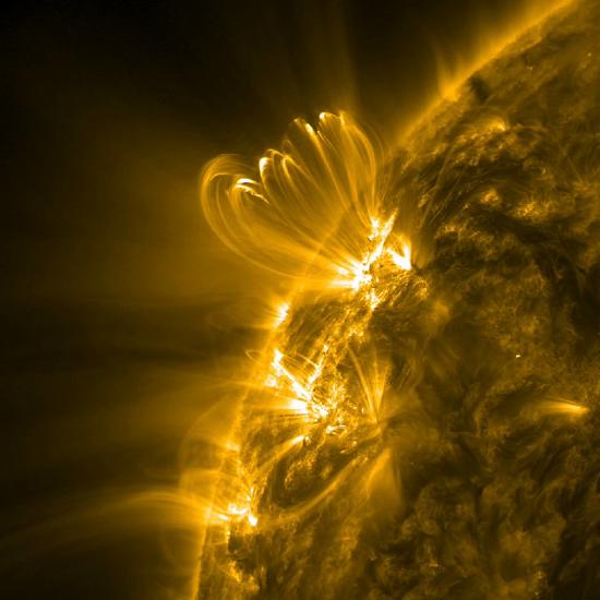 A partial view of the sun focusing on the eruption of a solar flare in bright yellow. The solar flare expands beyond the layer of the sun photographed.