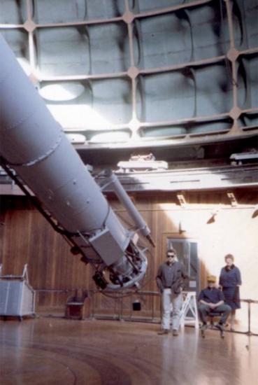 Three people pose near the bottom end of a cylinder-shaped object inside an observatory dome.