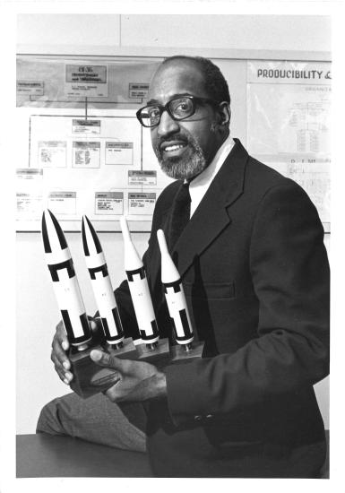 Frank Crossley, an African-American man, sits with a set of trophies featuring rocket figurines.