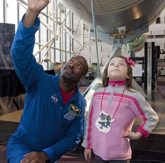 Former Astronaut Leland Melvin, an African-American man, kneels next to a young child at the Museum.