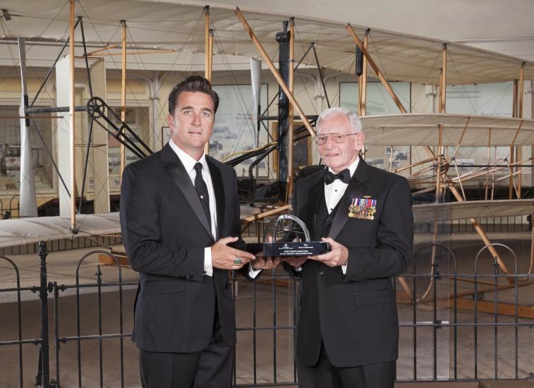 Dr. Adam Steltzner and Gen. Jack Dailey, two white men, pose for a photo as Steltzner accepts a trophy.