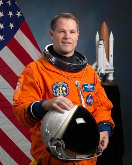 Commander Kevin Ford, a white male astronaut, poses for his official astronaut portrait in an orange suit. He is holding an astronaut helmet.