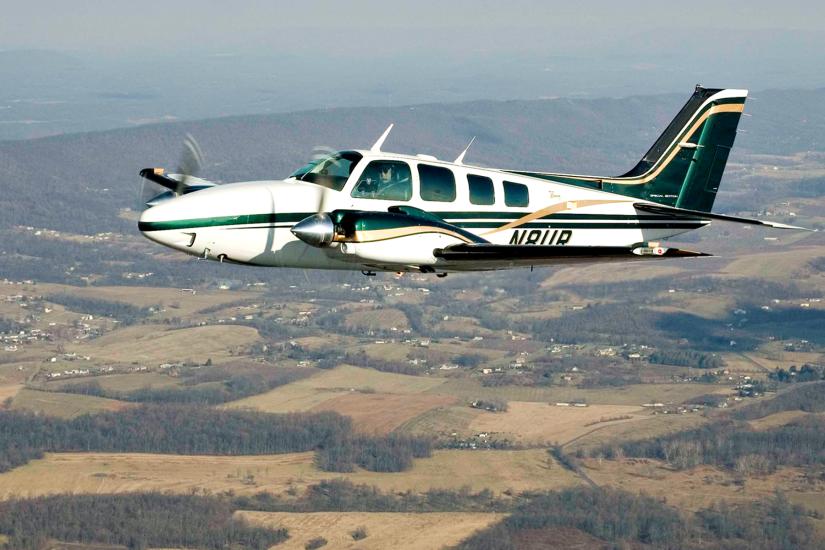 Side view of a white and green monoplane with twin engines in flight. The registration number "N8UR" is painted in a dark color near the rear of the fuselage.