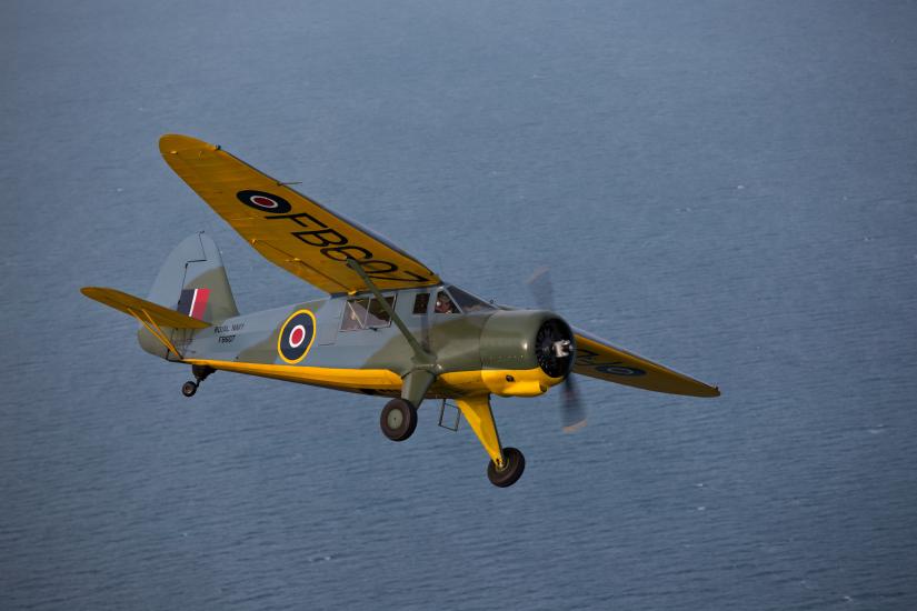 Side view of yellow, olive drab green, and gray monoplane in flight with one engine and fixed landing gear.