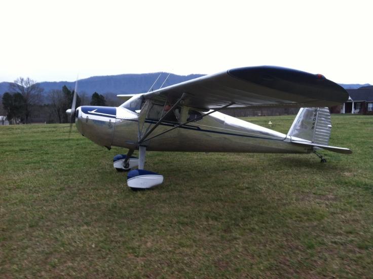 Side view of white and blue monoplane with single engine and fixed landing gear.