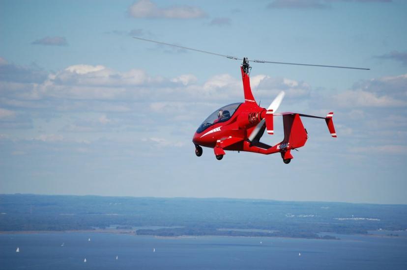 Side view of a small red helicopter in flight with one two-blade propellor above the cockpit.