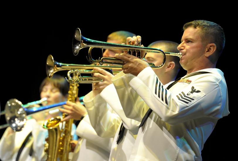 A group of performers in U.S. Navy uniforms play various instruments.