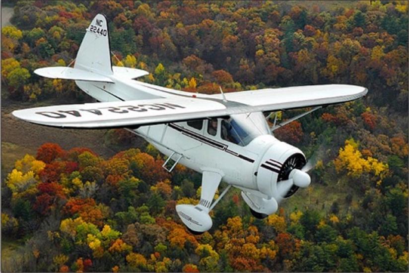 Diagonal front view of a white monoplane in flight with fixed landing gear and one engine.