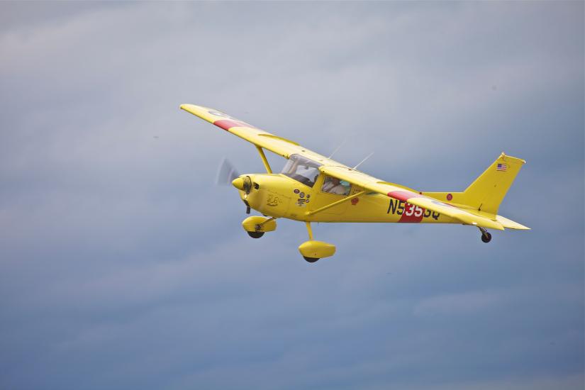 Side view of yellow monoplane in flight with single engine and fixed landing gear.