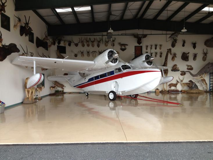 Side view of white and red amphibious aircraft with twin engines and one pontoon on each wing.