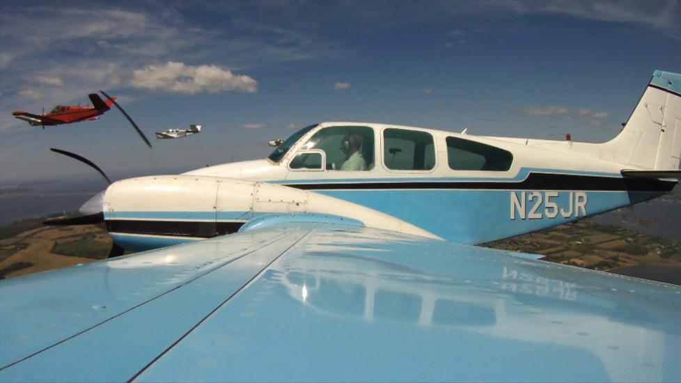 Side view of white and light blue monoplane in flight with twin engines. Registration number "N25JR" is painted in white near the rear of the fuselage.