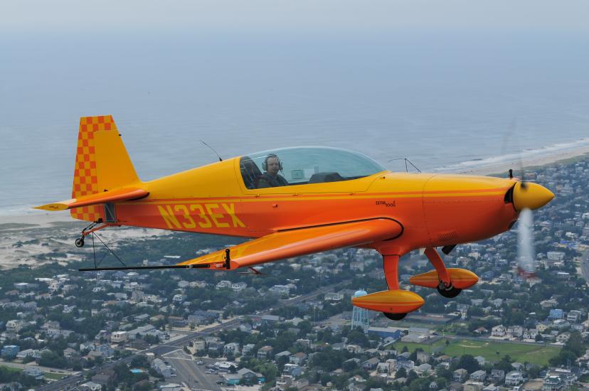 Side view of yellow and orange monoplane with single engine and fixed landing gear. Registration number "N33EX" is painted in yellow behind the cockpit.