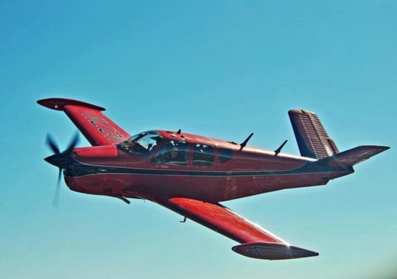 Side view of red and black monoplane in flight with single engine.