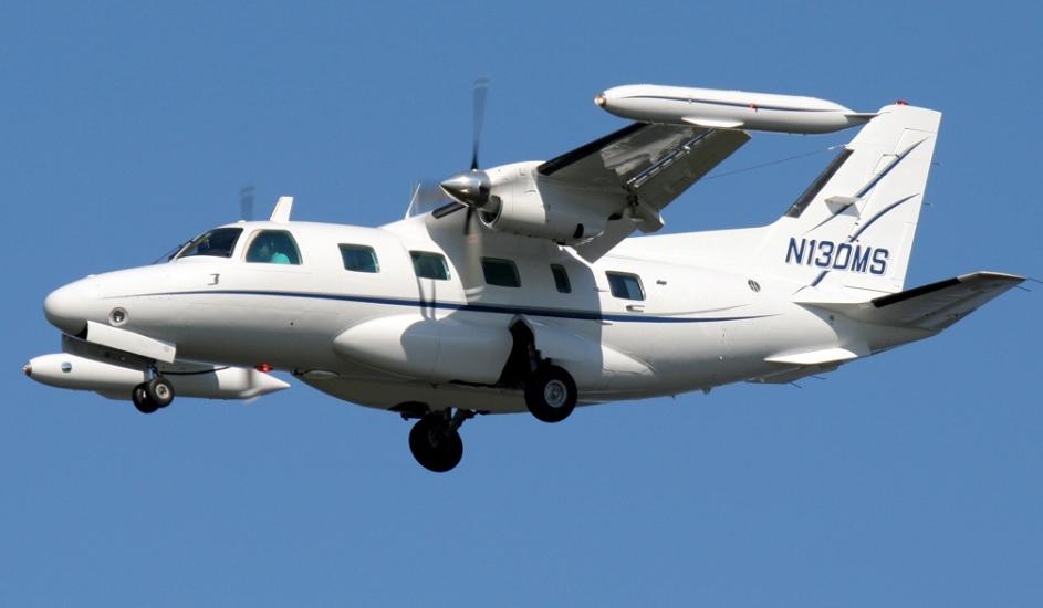 Side view of white monoplane in flight with twin engines. Registration number "N130MS" is painted in blue on the vertical stabilizer.