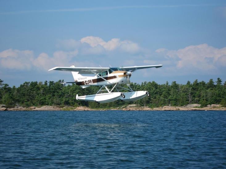 Front view of a white amphibious aircraft with single engine and pontoon floats below the fuselage.