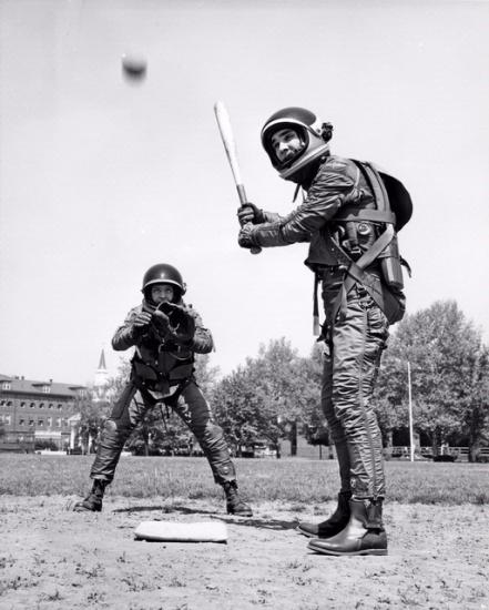 Two people play baseball in suits intended for use in space.