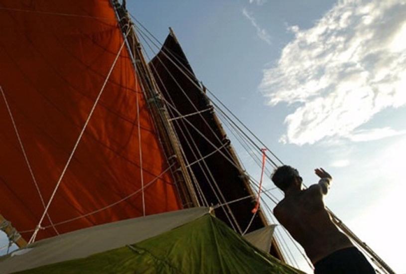 A person on a sailboat uses their hands to determine direction.