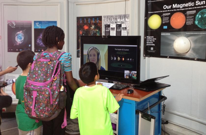 Three museum visitors speak with a museum expert who chats with them through video chat on a computer.