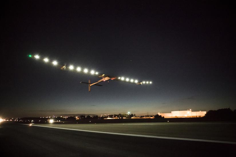 A plane with very long wings lined by lights departs an airport.