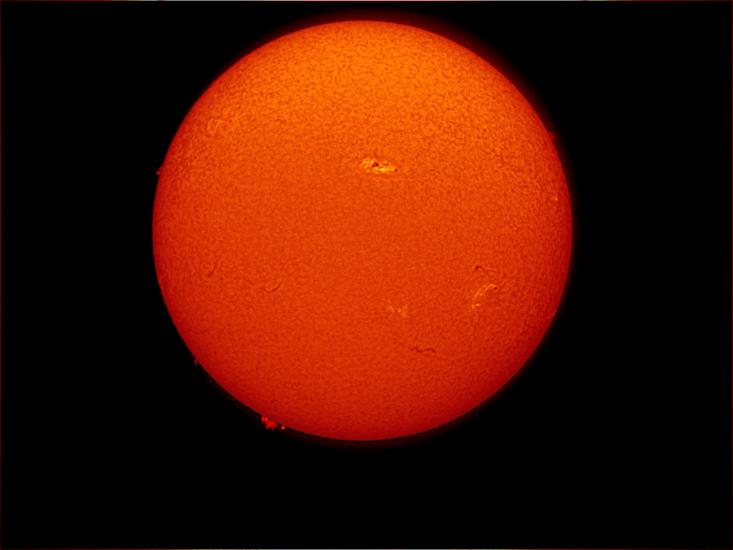 Disk view of the Sun's atmosphere. This image features sunspot clusters (dark spots) surrounded by phages (lighter colored clouds). Filaments (gases floating above the surface) are visible as dark lines on the visible disk, as well as prominences (gases floating from the surface) off the edges of the disk.