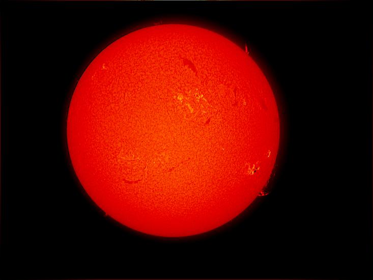 Disk view of the Sun's atmosphere. This image features sunspot clusters (dark spots) surrounded by phages (lighter colored clouds). Filaments (gases floating above the surface) are visible as dark lines throughout the visible disk, as well as prominences (gases floating from the surface) off the edges of the disk on the right side.