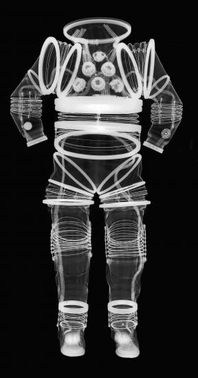 Negative x-ray of the front view of an early, experimental full-body spacesuit. Full flexibility can be seen in joint regions through the spring-like appearance of white lines around joints.