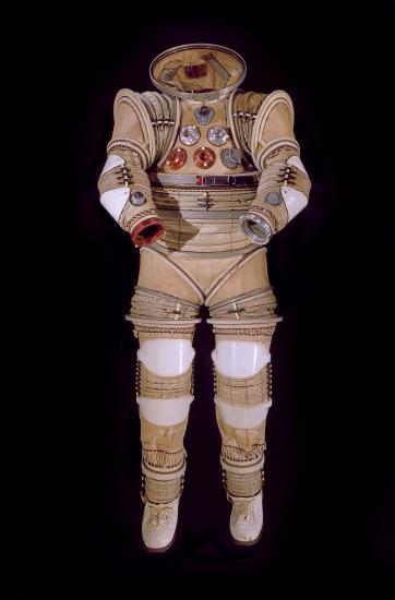 Front view of tan and translucent white full-body experimental spacesuit. Spaces for not present helmet and gloves are open.