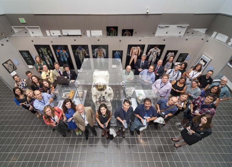 A large group of people stand around an museum exhibit featuring spacesuits.