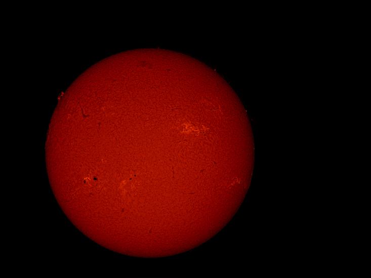 Disk view of the Sun's atmosphere featuring some sunspots (dark spots on the sun) surrounded by lighter-colored phages and a solar flare. A prominence and filament are visible as floating red gases on the upper left edge and a dark line on the upper center of the Sun, respectively.