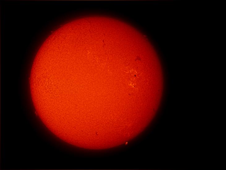 Disk view of the Sun's atmosphere. One sunspot cluster is visible as a dark spot on the Sun surrounded by lighter clouds called phages on the right side of the disk.