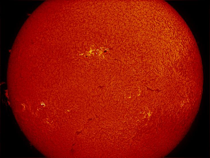 Partial disk view of the Sun's atmosphere. A sunspot group of dark spots is visible in the center of the image and is surrounded by lighter-colored phages. Filaments (dark lines) and phages are also visible on the lower half of the disk.