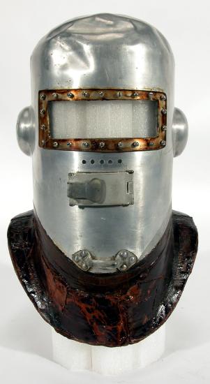 A primitive pressure helmet which looks like a knight's helmet with metal full-body face guard and darker-colored brim for attachment to the rest of a pressurized suit.