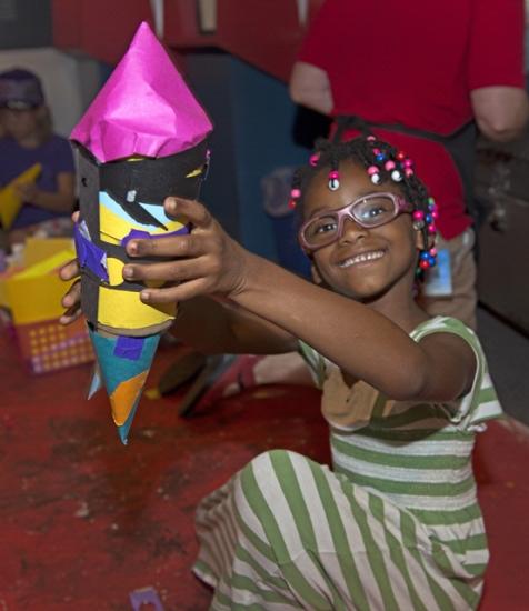 A young girl displays her colorful, finished art project during a family event at the museum.