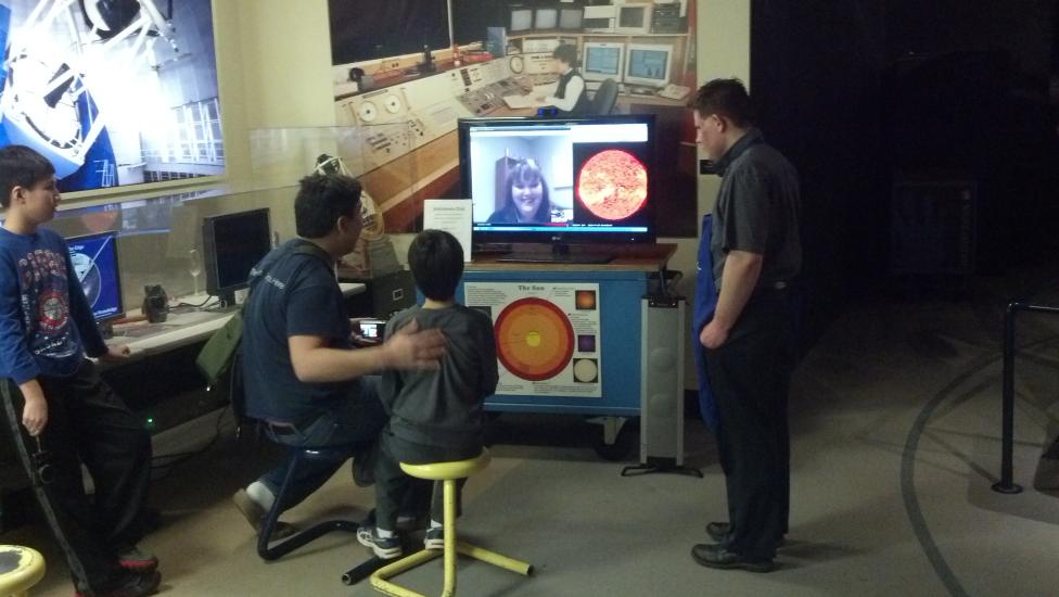 Four museum visitors video chat with a museum expert on astronomy inside the Museum's observatory.