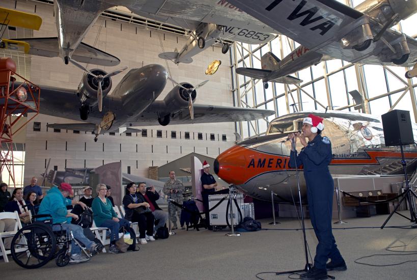 A musician from the U.S. Air Force performs as part of a band at the Museum. They are wearing a red and white Santa hat.